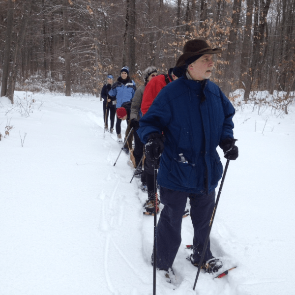 Hikers in single file line walk toward the photographer across ground covered by snow